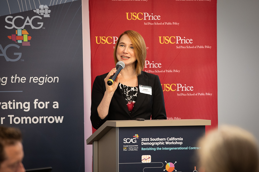 Woman speaking at a podium, red and blue banners in background.