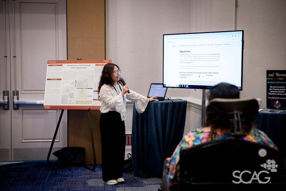 Presenter with microphone near a screen in a conference room.