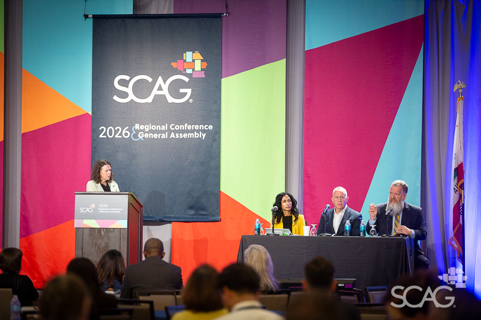 Panelists on stage at a colorful conference backdrop with SCAG logo.