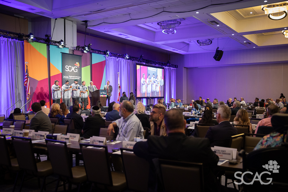 Conference event with seated attendees, colorful stage, and presentation screen.