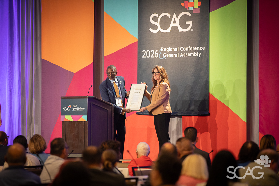 Award presentation at SCAG conference with a colorful geometric backdrop.