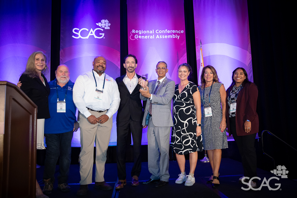Eight people on stage smiling against a purple backdrop with "SCAG" logos.