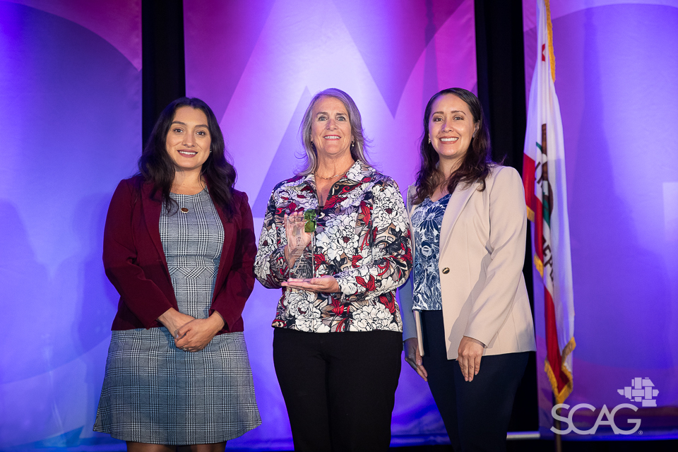 Three women standing together, smiling, with a purple backdrop.