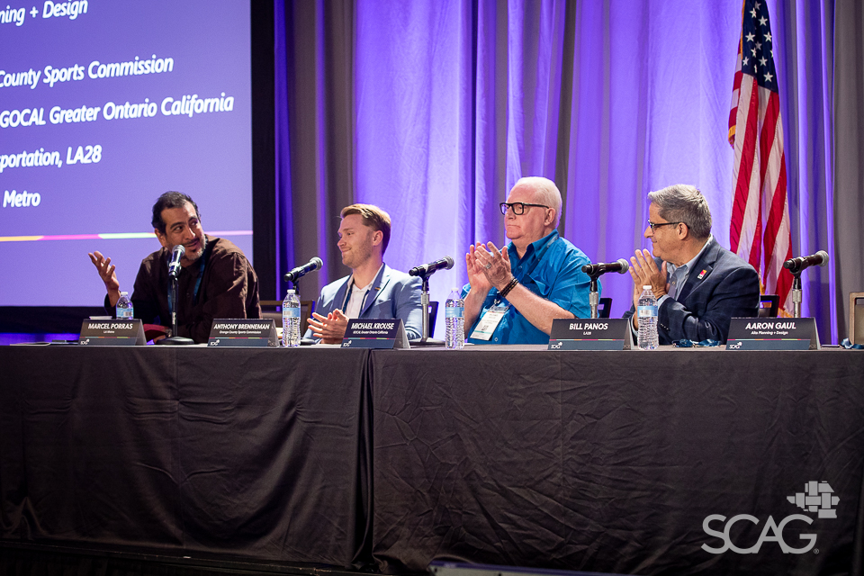 Panelists sit at a table with microphones and water bottles, engaged in discussion.