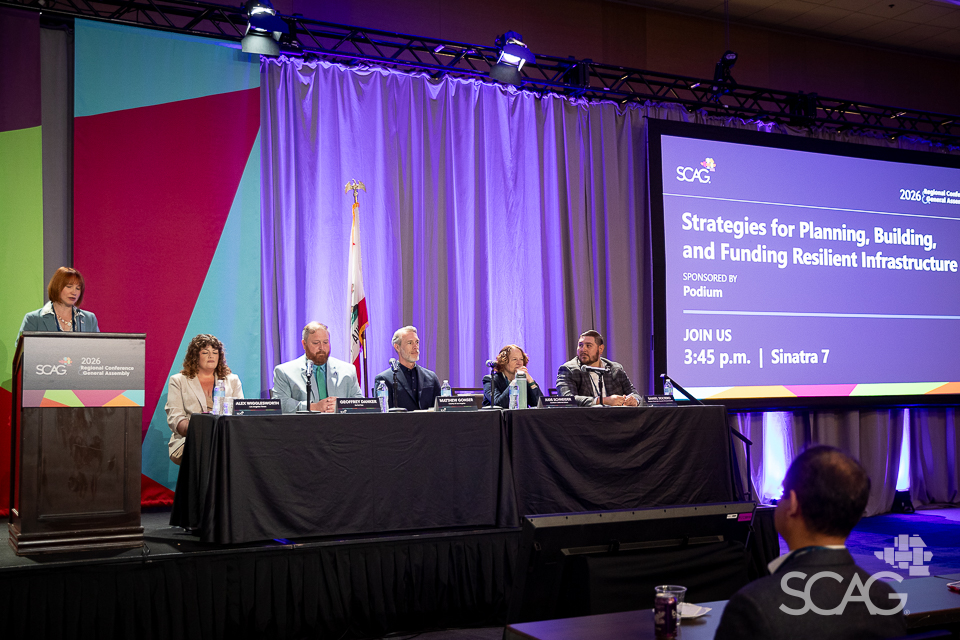 Panel of six people at a conference with purple-lit stage.