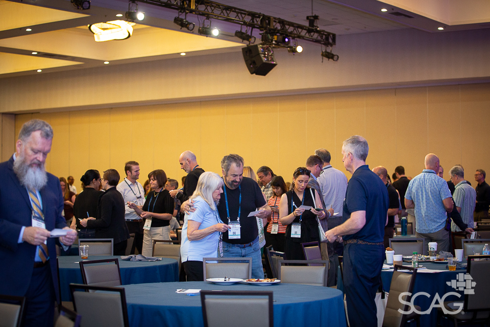 Conference attendees networking in a large room with round tables.