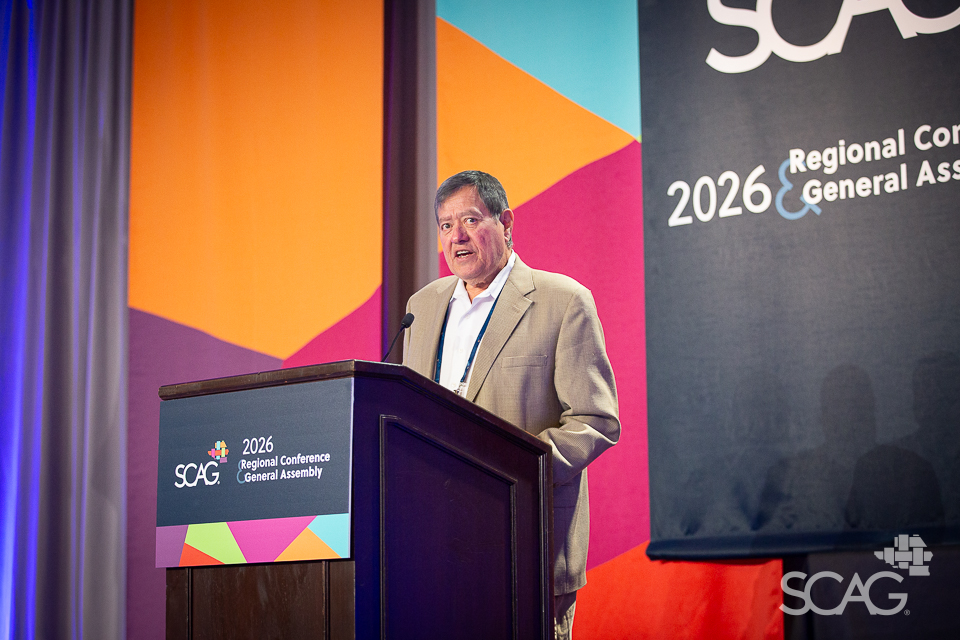 Man in a suit speaking at a podium with colorful backdrop.