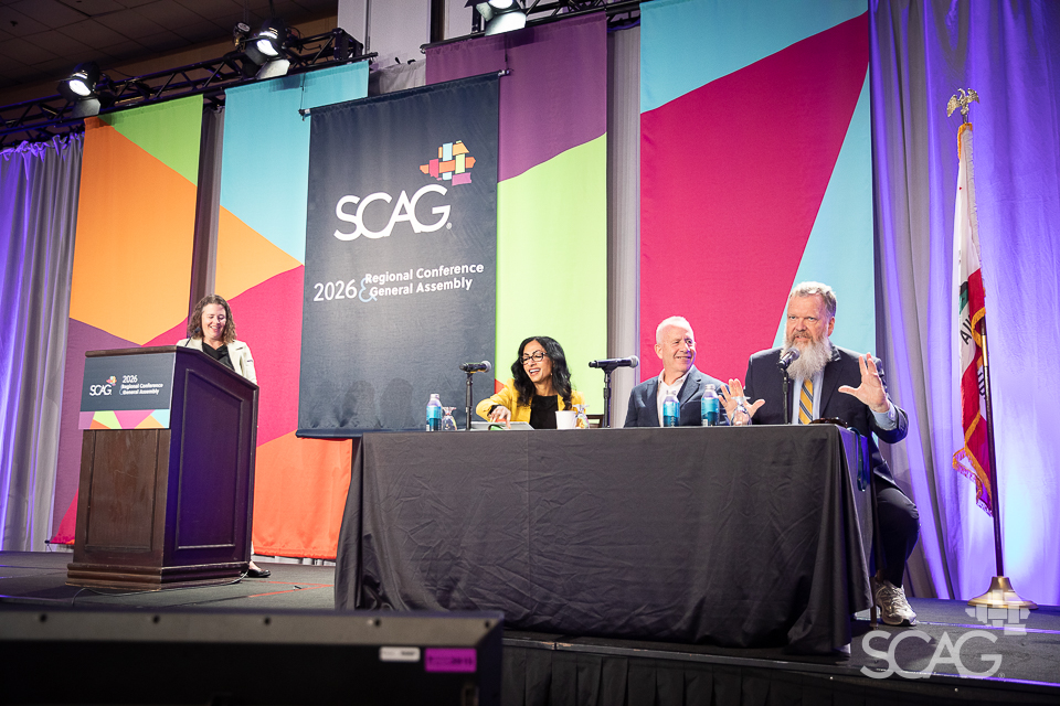 Panelists speaking at a conference with colorful backdrop and SCAG logo.