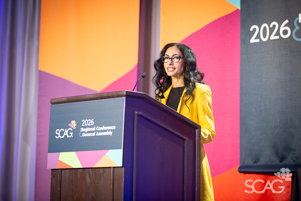 Woman speaking at a podium in a conference setting with colorful backdrop.
