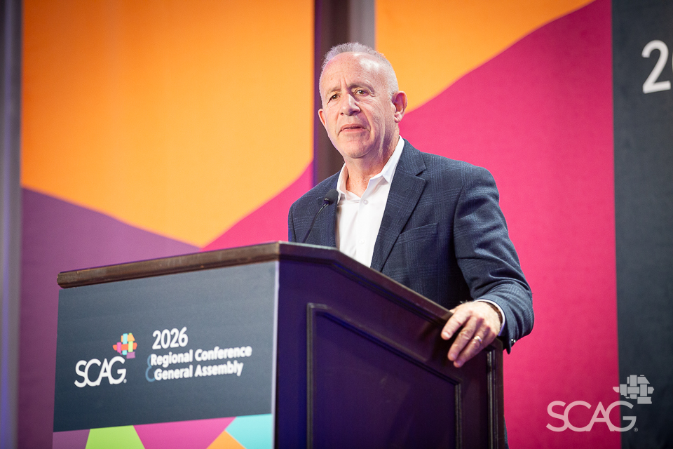 Man in suit speaking at a conference podium with colorful backdrop.