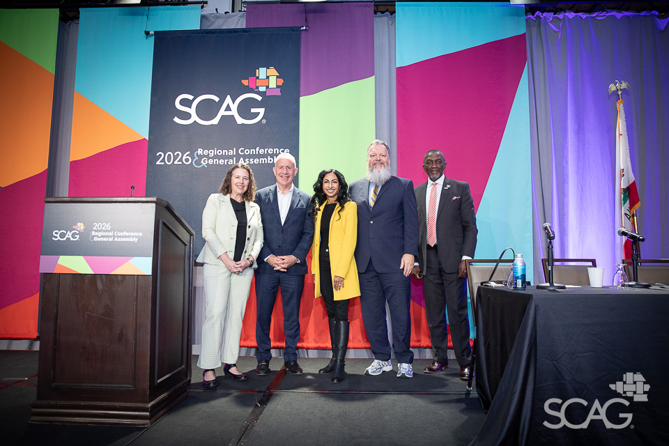 Five people posing in front of a colorful stage backdrop at a conference.