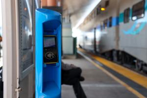 Blue ticket validator at a train platform, blurred train in the background.