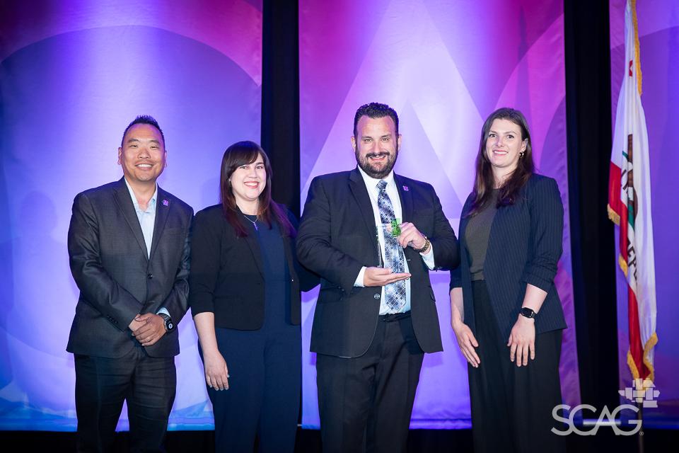 Four people in suits smiling on stage with a purple background.