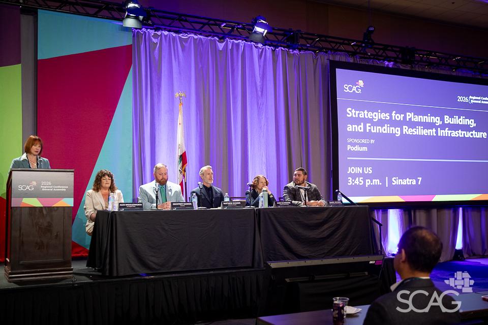 Panel of six people at a conference with purple-lit stage.