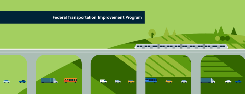 Train on a bridge above cars and trucks on a road, green hills in the background.