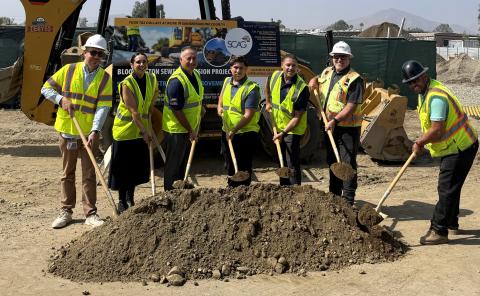 Workers in safety vests holding shovels at a groundbreaking ceremony.