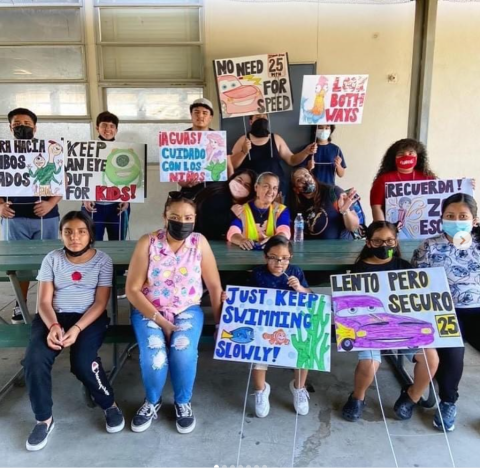 Kids and adults holding colorful protest signs while seated at a table.
