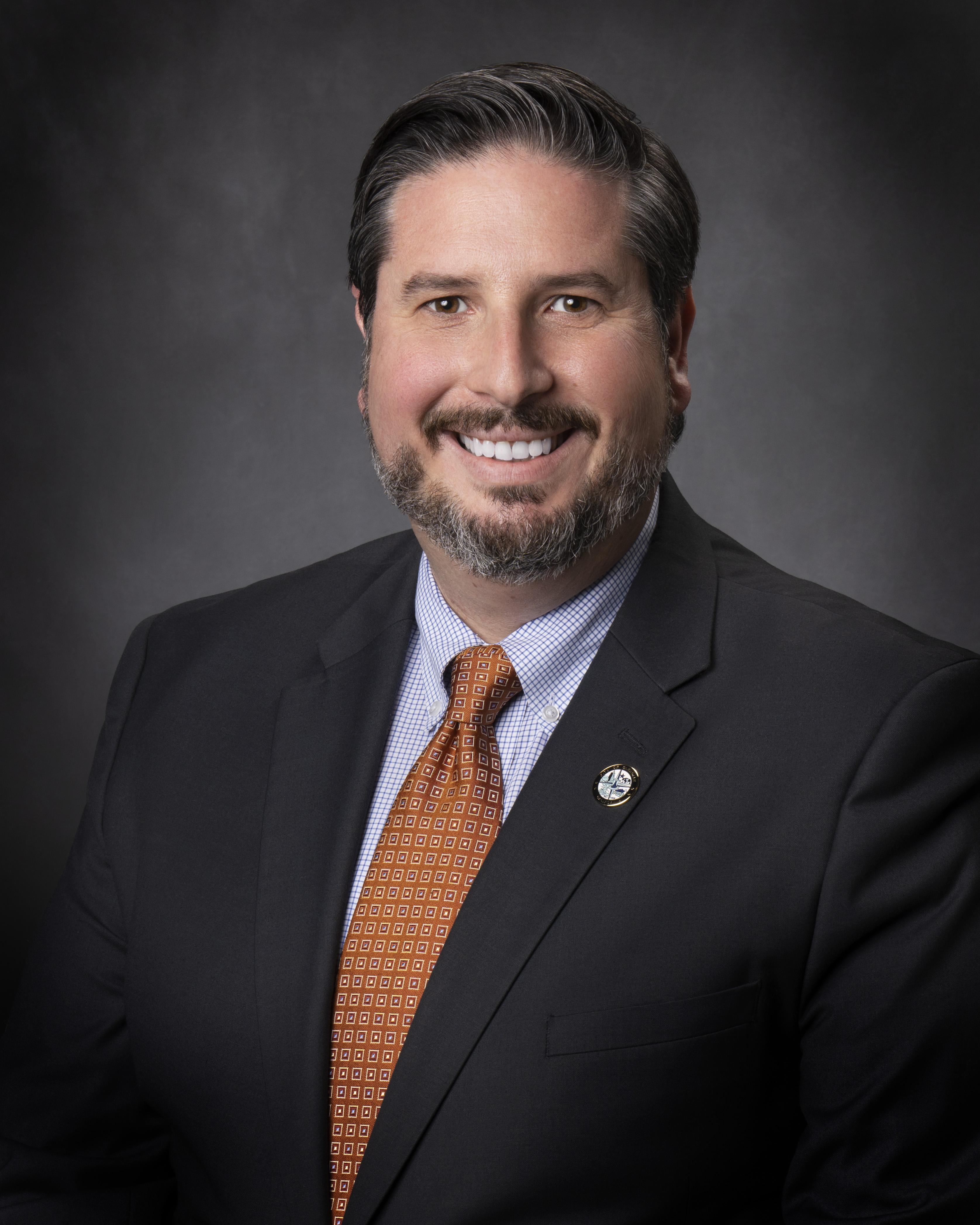 Smiling man in a suit with a striped tie, neutral background.
