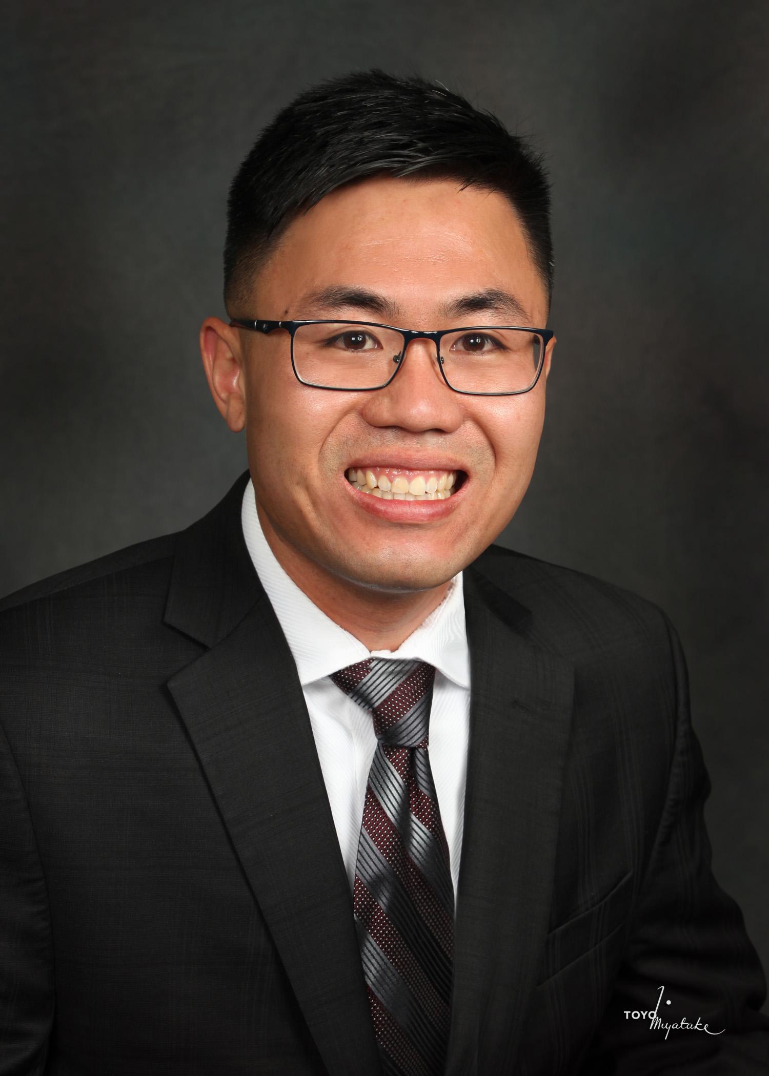 Smiling man in a suit and tie against dark background.